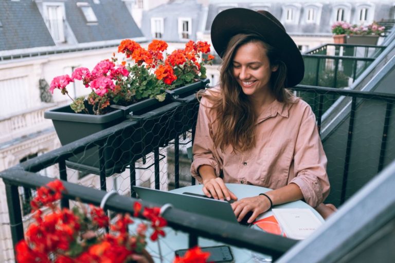 Frau-mit-Hut-auf-Balkon-mit-Blumen